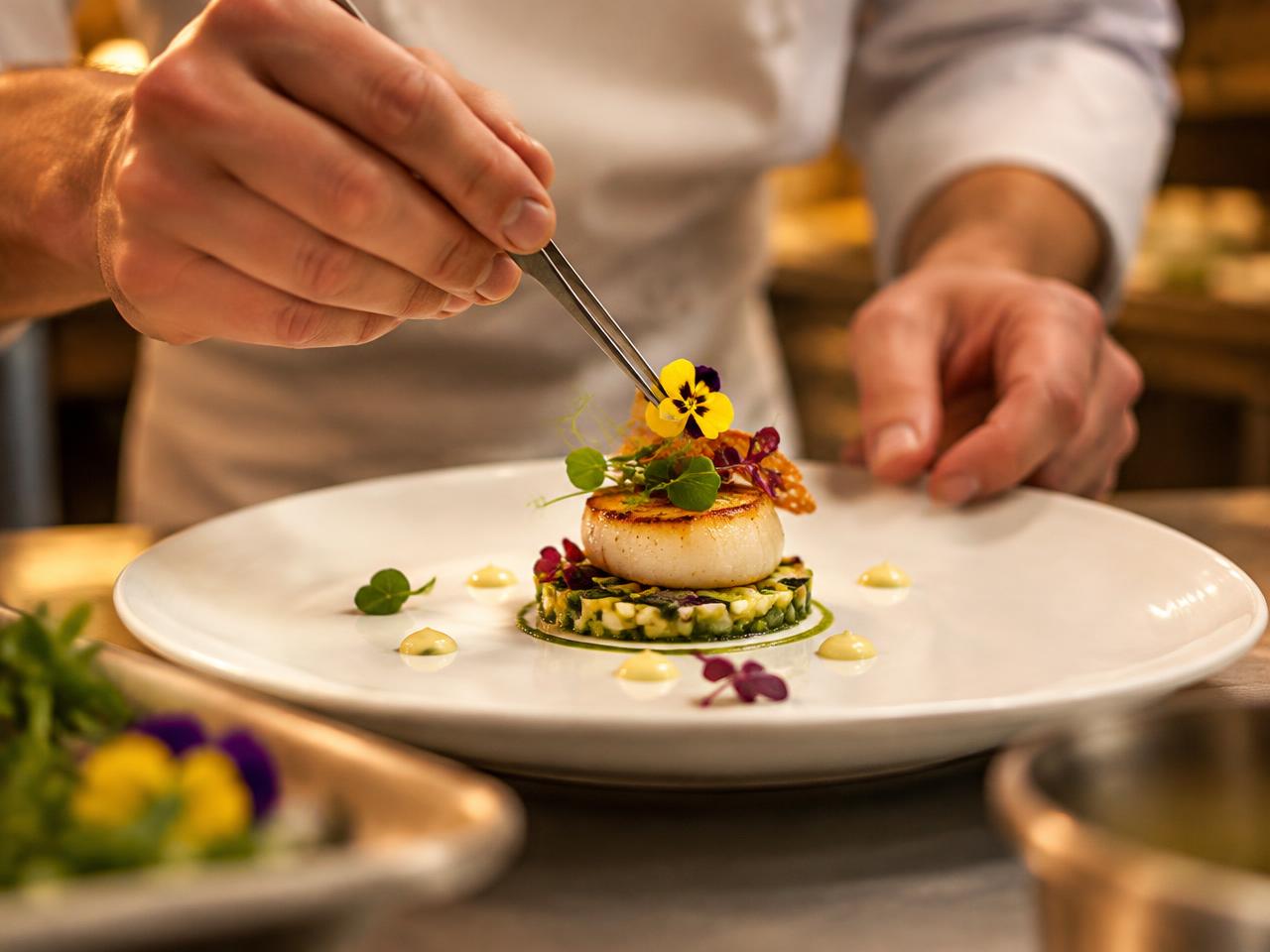 A chef garnishing a plated appetizer with edible flowers